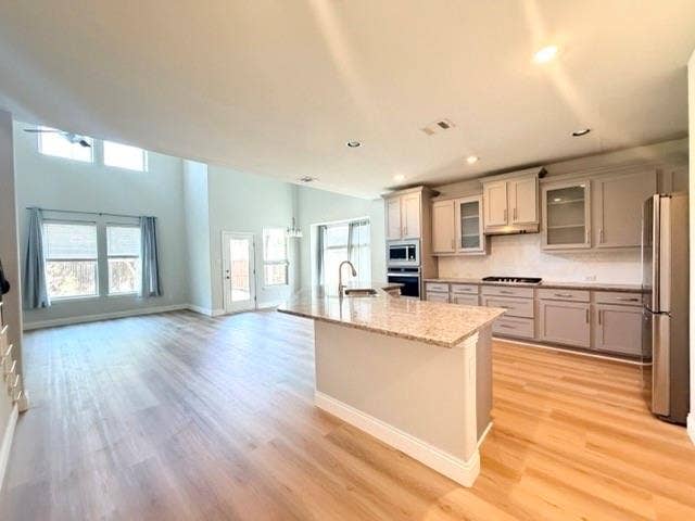 5609 Meritage Street, McKinney, TX 75070 Open-concept living space featuring wood-finish flooring, a kitchen island with stone countertop, stainless steel appliances, and a vaulted ceiling with transom windows