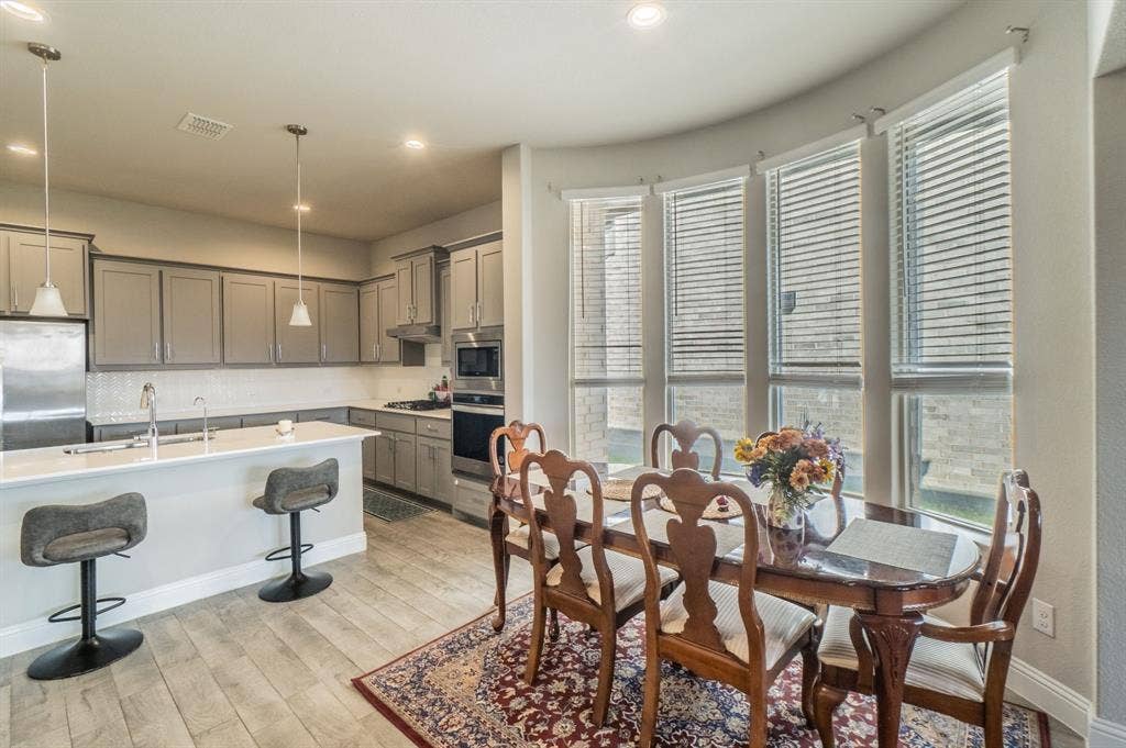 2041 St Andrews Way, Argyle, TX 76226 Kitchen and dining area featuring wood-finish flooring, recessed lighting, pendant lighting, built-in stainless steel appliances, and a curved wall of windows
