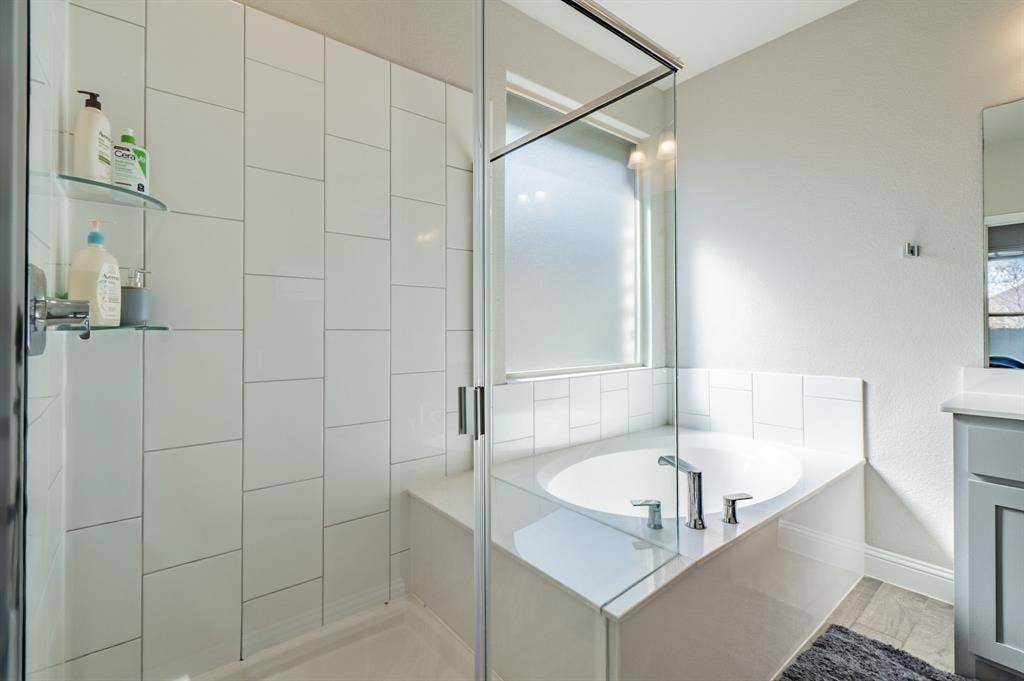 2041 St Andrews Way, Argyle, TX 76226 Glass-enclosed shower with white tiled walls, built-in bench, and dual glass shelves