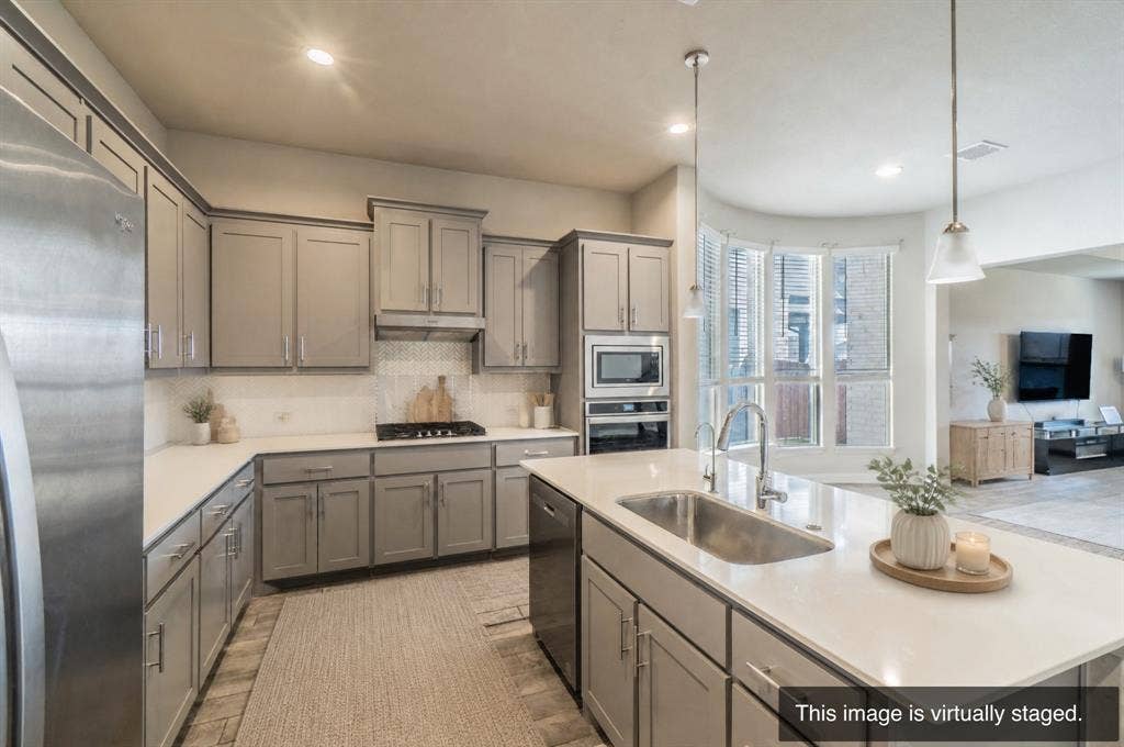 2041 St Andrews Way, Argyle, TX 76226 Kitchen featuring a central island with an undermount sink, pendant lighting, white countertops, stainless steel appliances, and gray cabinetry