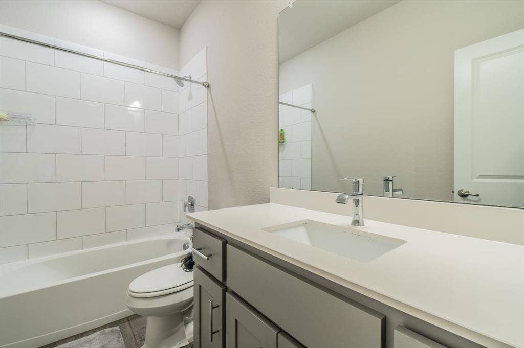 2041 St Andrews Way, Argyle, TX 76226 Bathroom featuring a white subway tile shower, white bathtub, gray vanity with an integrated sink, and a chrome faucet