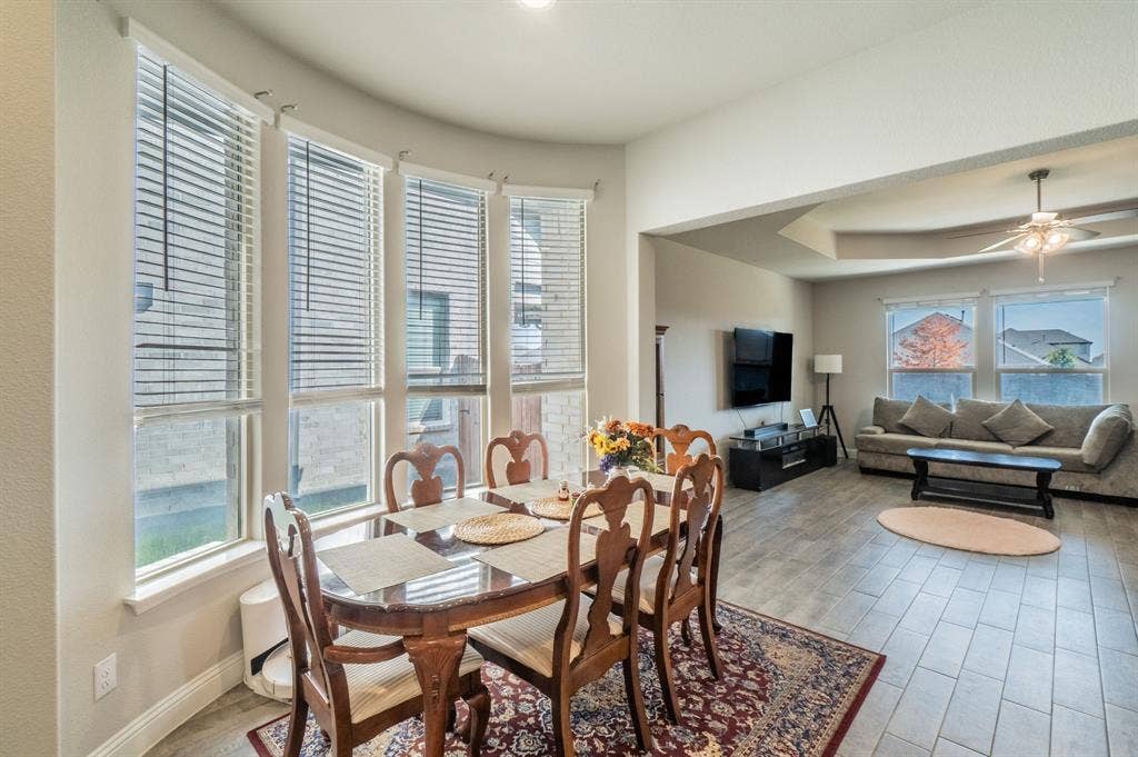 2041 St Andrews Way, Argyle, TX 76226 Bay window with multiple vertical blinds, recessed ceiling lighting, wood-finish flooring, tray ceiling with a mounted ceiling fan, and large windows