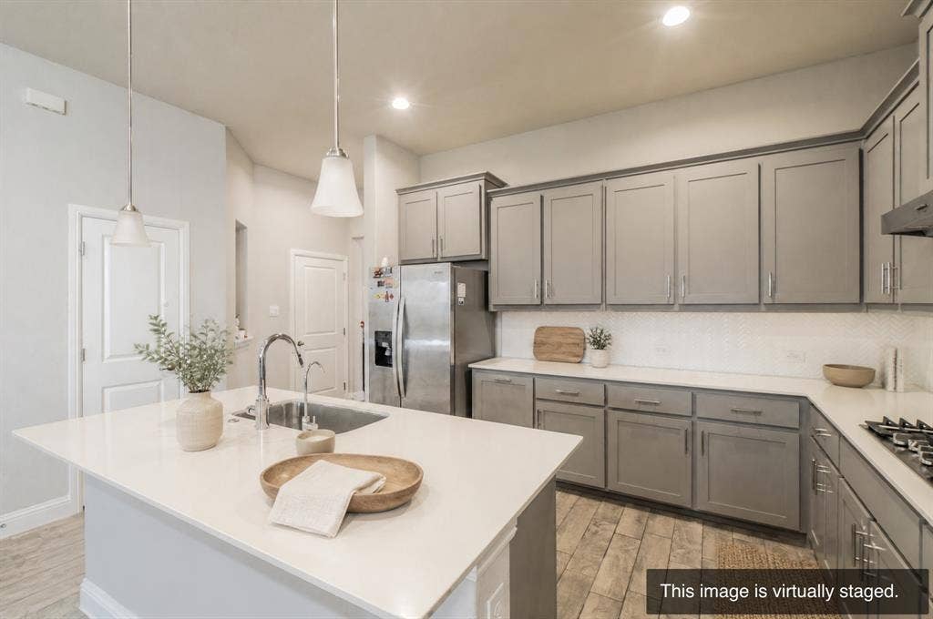 2041 St Andrews Way, Argyle, TX 76226 Kitchen featuring a central island with an undermount sink, pendant lighting, gray shaker-style cabinetry, stainless steel appliances, and wood-finish flooring