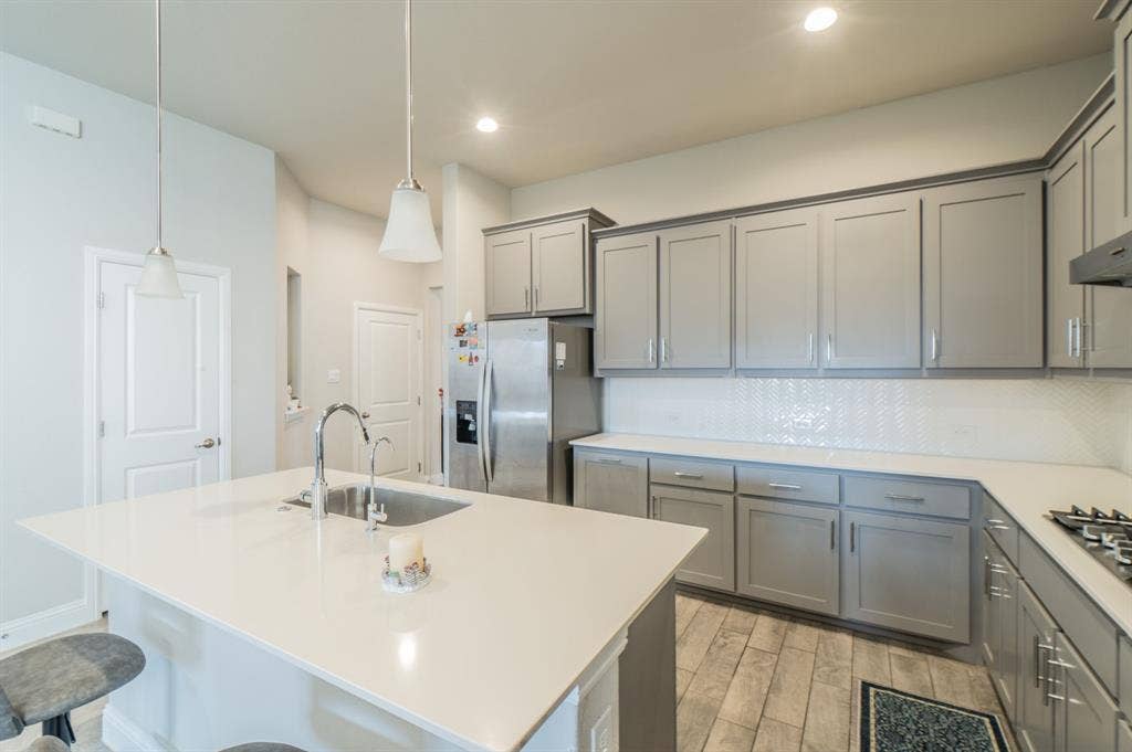 2041 St Andrews Way, Argyle, TX 76226 Kitchen featuring light gray cabinetry, white countertops, stainless steel appliances, a white herringbone tile backsplash, and wood-finish flooring