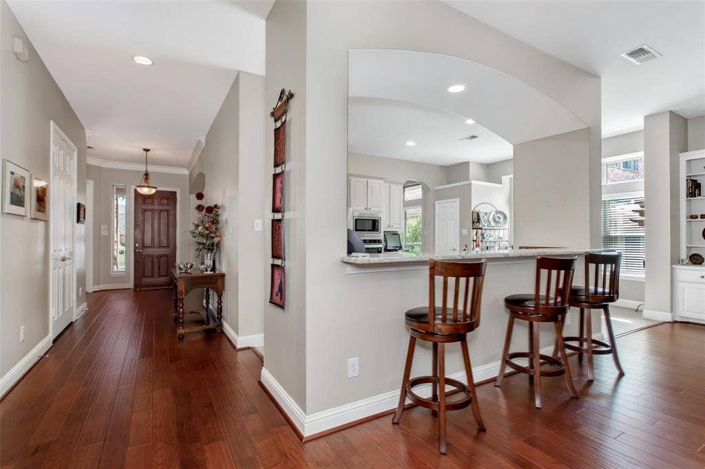 Wood-finish flooring throughout, arched kitchen pass-through, recessed lighting, and a paneled entry door with sidelight