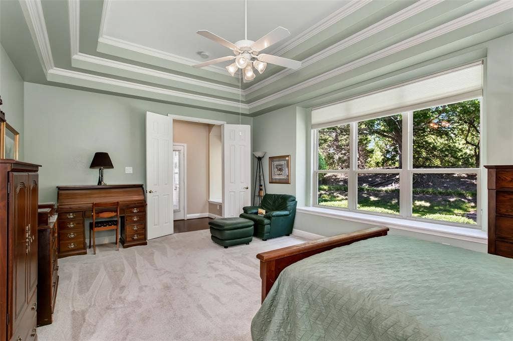 Tray ceiling with decorative molding, large multi-pane window, light-toned carpet, recessed lighting, and ceiling fan