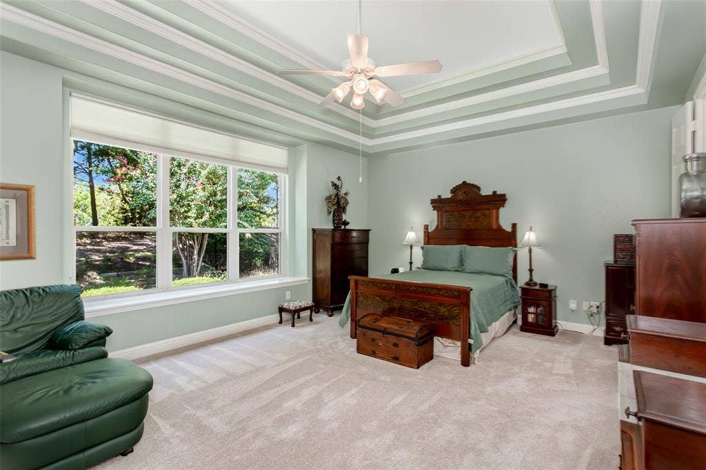 Tray ceiling with crown molding, ceiling fan, large window with sills, and carpeting