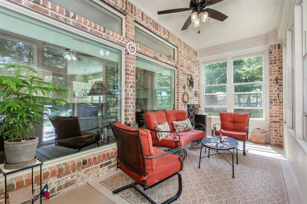 Brick-accented sunroom with large windows, transom windows, a ceiling fan with light fixture, and a screened enclosure