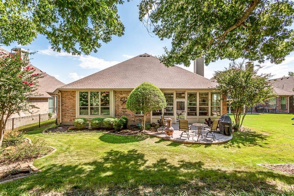 Expansive backyard with a manicured lawn, brick exterior, and a built-in patio