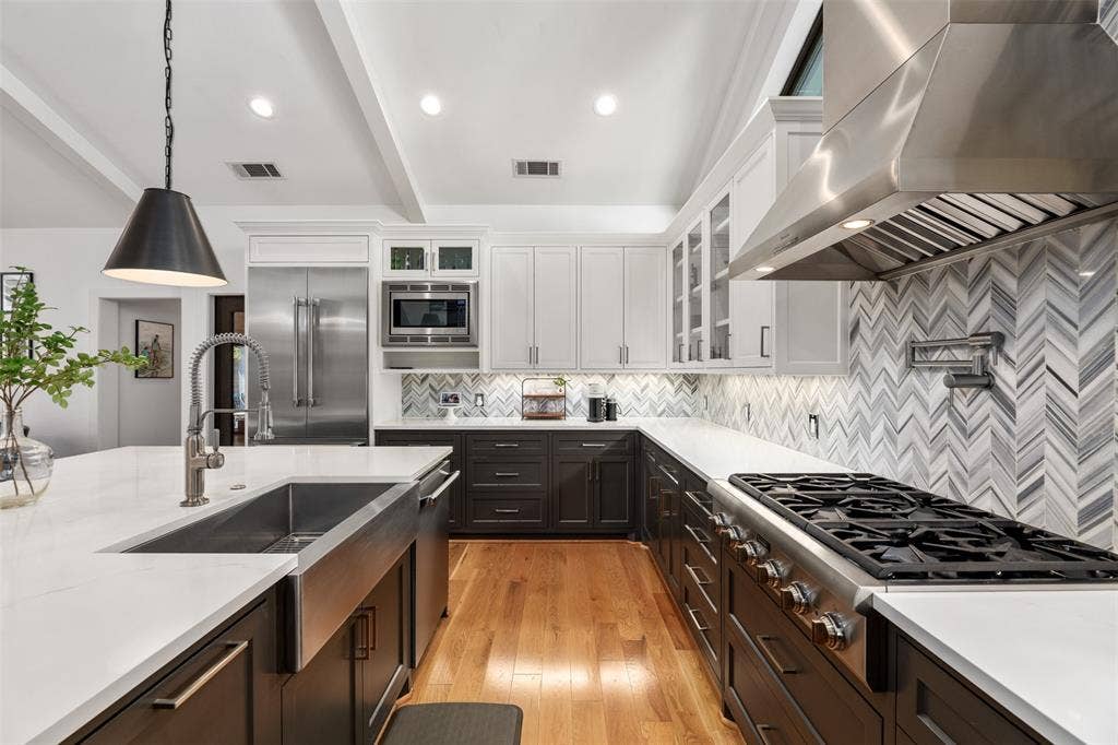 Gourmet kitchen with stainless steel appliances, white countertops, two-tone cabinetry, wood-finish flooring, and a chevron pattern backsplash