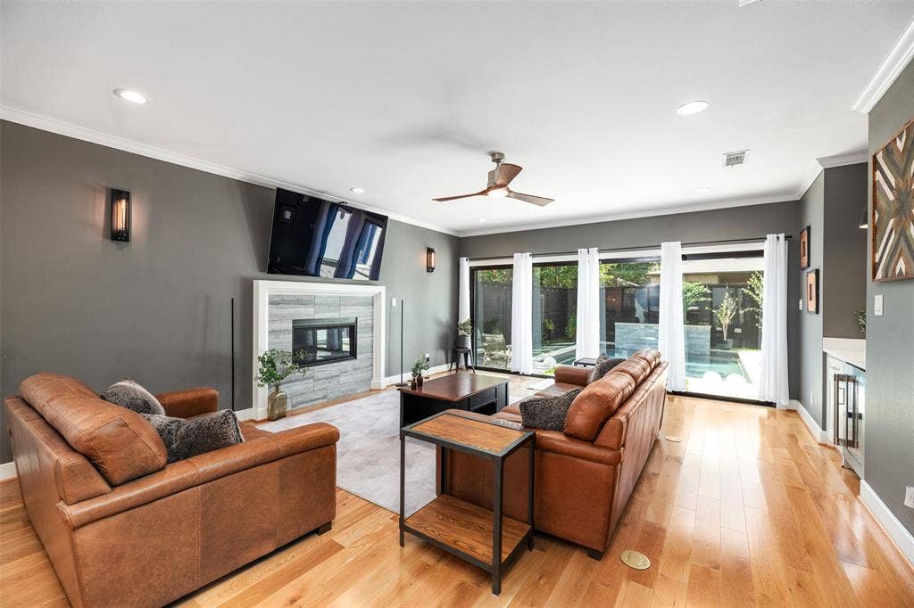 Living area featuring a fireplace with stacked stone surround, wood-finish flooring, a ceiling fan, recessed lighting, and expansive glass doors opening to a backyard