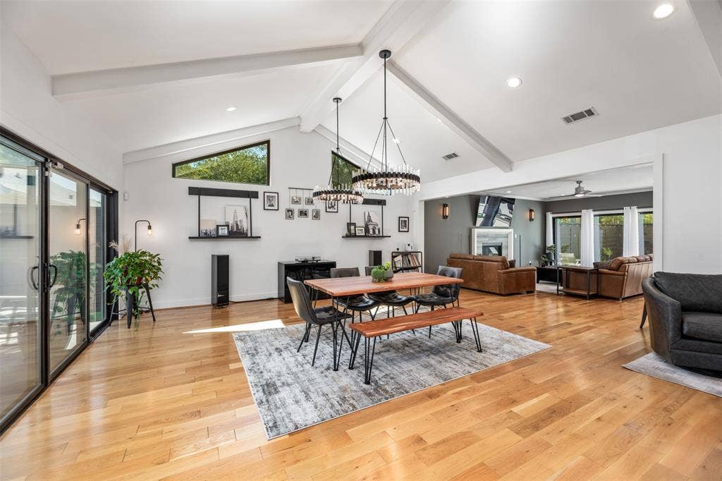 Vaulted ceiling with exposed beams, wood-finish flooring, recessed lighting, and expansive glass sliding doors
