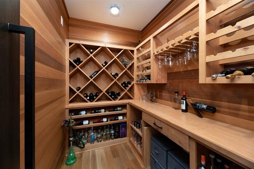 Custom wood-paneled walls, built-in wine storage, integrated glass rack, rich wood-finish flooring, and recessed ceiling lighting