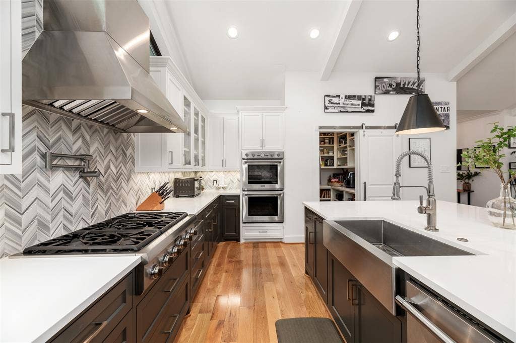 Kitchen featuring hardwood flooring, dual-tone cabinetry, stainless steel appliances, a chevron-patterned tile backsplash, and an island with a farmhouse sink