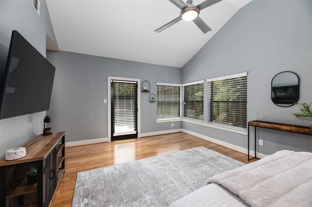 Vaulted ceiling with a ceiling fan, wood-finish flooring, multiple windows with blinds, and a glass-paneled door
