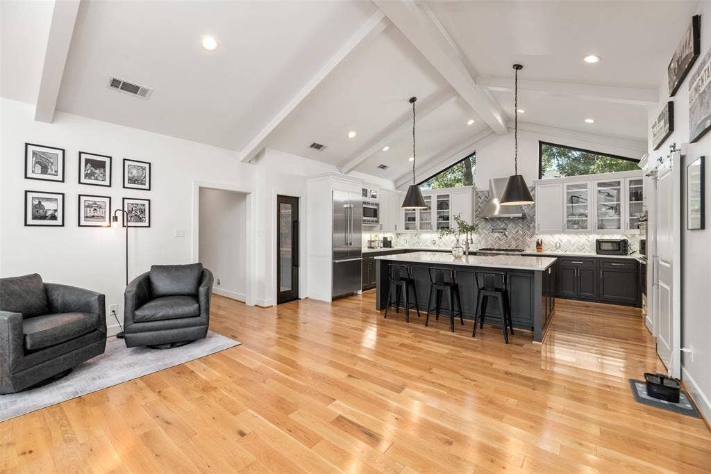 Vaulted ceiling with exposed beams, wood-finish flooring, two-tone cabinetry, stainless steel appliances, and a large center island
