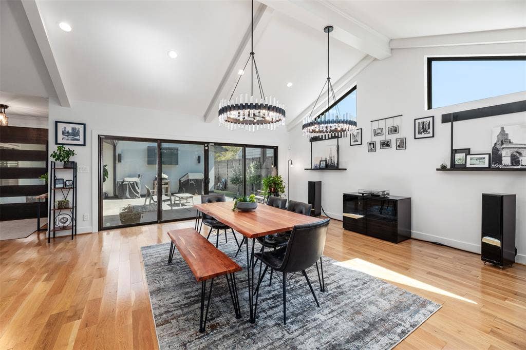 Vaulted ceilings with exposed beams, wood-finish flooring, two contemporary chandeliers, and expansive sliding glass doors