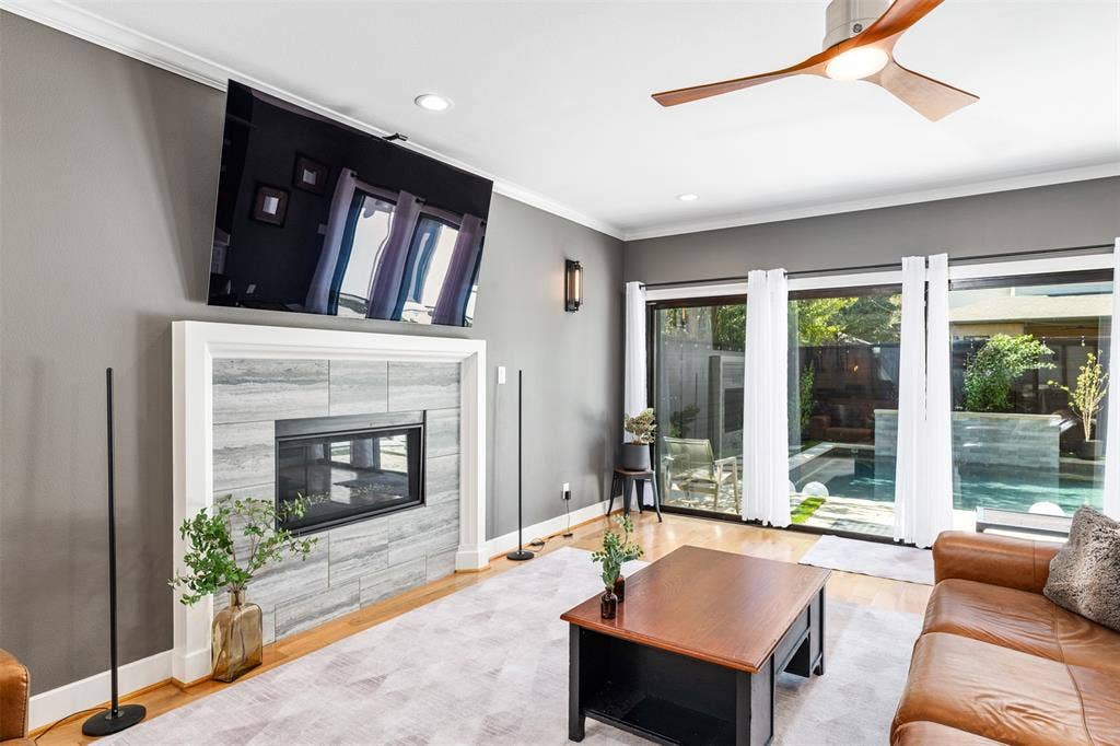 Gas fireplace with stone surround, wood-finish flooring, recessed lighting, modern ceiling fan, and sliding glass doors