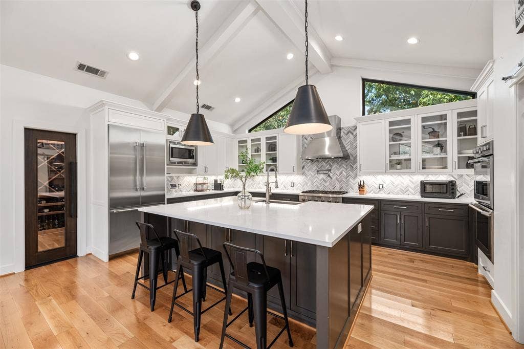 Kitchen featuring vaulted ceilings, wood-finish flooring, a central island with a light-toned countertop, stainless steel appliances, and a herringbone pattern tile backsplash