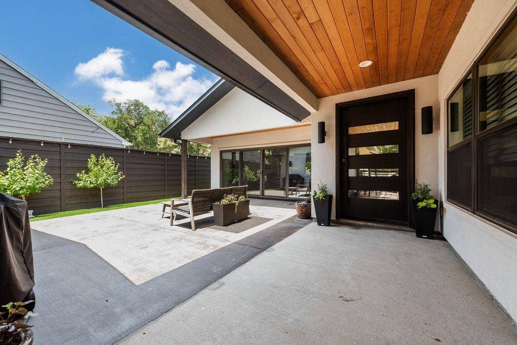Expansive concrete patio with a wood-planked ceiling and modern entry door featuring horizontal glass panels