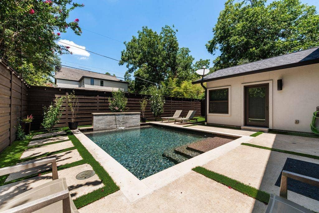 Private backyard oasis featuring a rectangular pool with integrated steps, a stone-finish water feature, and a privacy fence