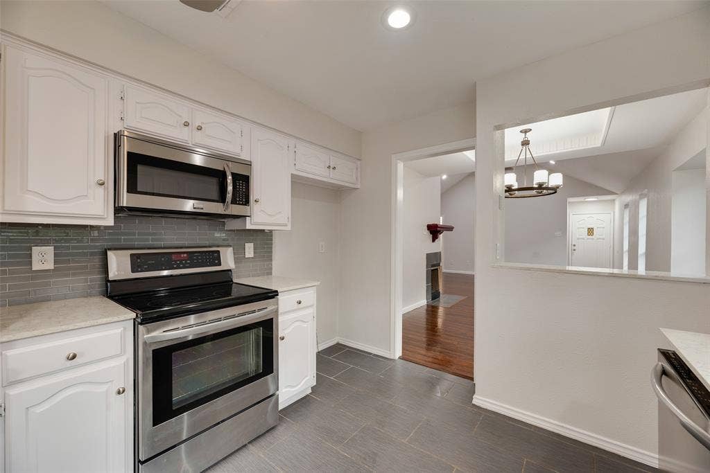 Stainless steel appliance suite, white cabinetry, tile backsplash, and stone-finish countertops