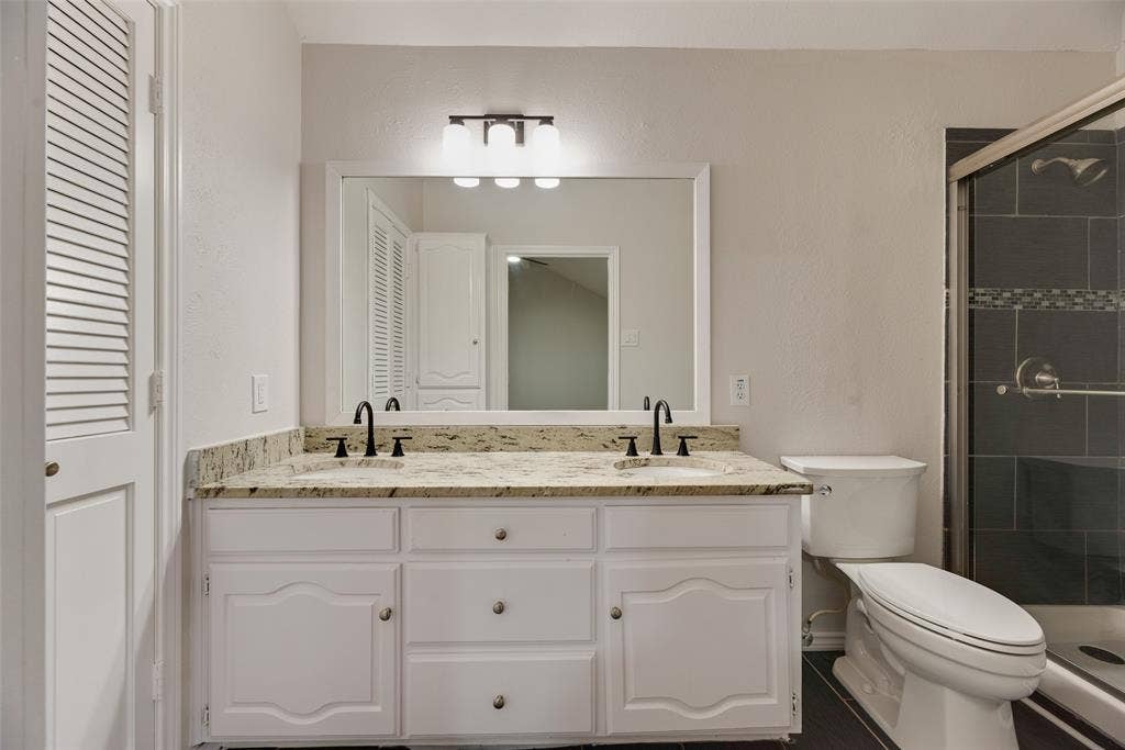 Dual vanity with granite countertop, white cabinetry, and matte black fixtures