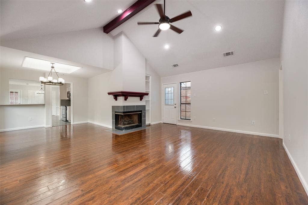 Vaulted ceiling with exposed beam, wood-finish flooring, recessed lighting, ceiling fan, and a tiled fireplace with wood mantel