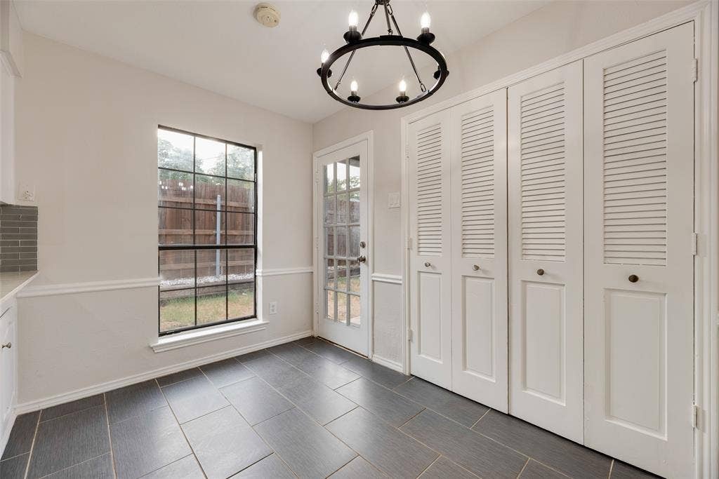 Dark tile flooring, white wainscoting, white louvered bifold doors, a glass-panel exterior door, and a black metal chandelier