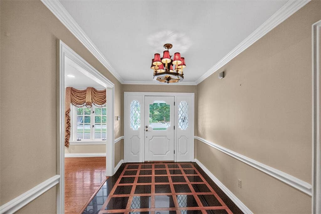 702 Mulberry Drive, Athens, TX 75751 Foyer featuring a decorative chandelier, white crown molding, and a patterned wood-finish floor