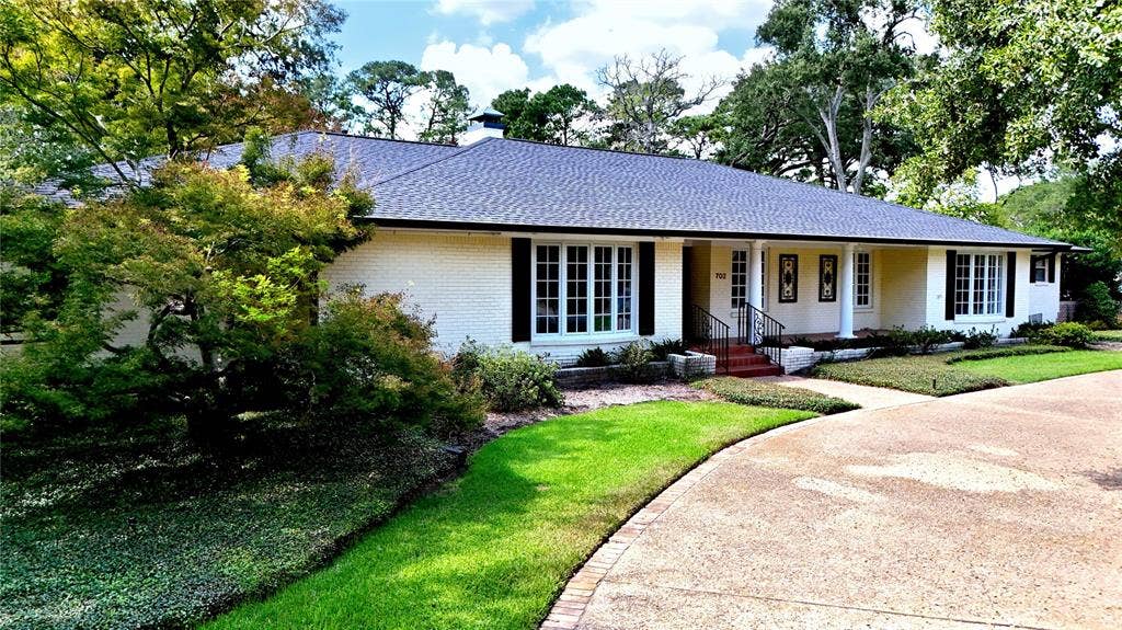 702 Mulberry Drive, Athens, TX 75751 Brick exterior, dark roof, front porch with columns, mature landscaping, and a paved driveway