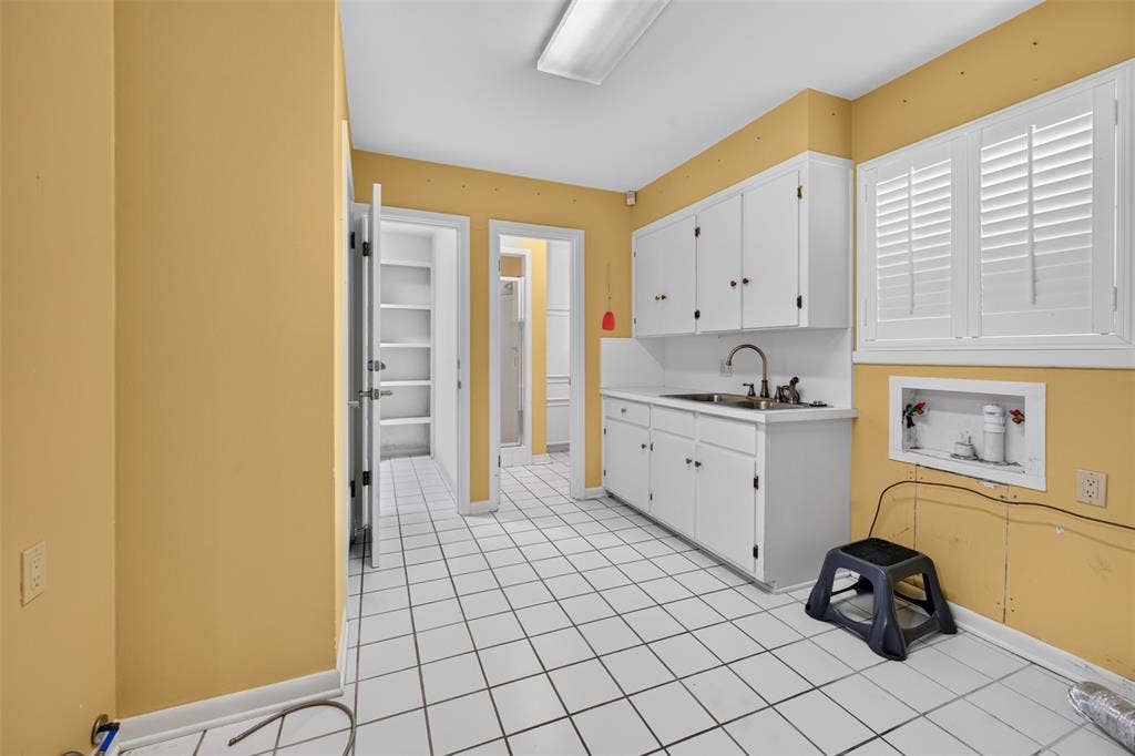 702 Mulberry Drive, Athens, TX 75751 White square tile flooring, white cabinetry, stainless steel sink, window with white plantation shutters, built-in shelving