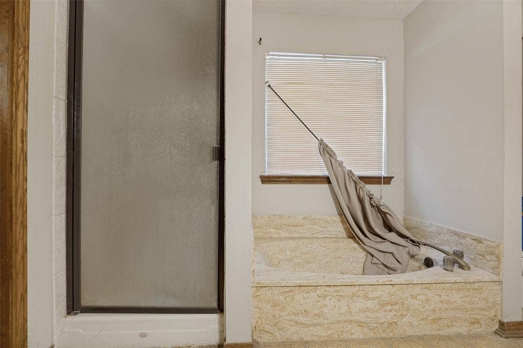 1901 Wedgewood Drive, Grand Prairie, TX 75050 Built-in soaking tub with stone surround, a window with horizontal blinds, and a glass-enclosed shower