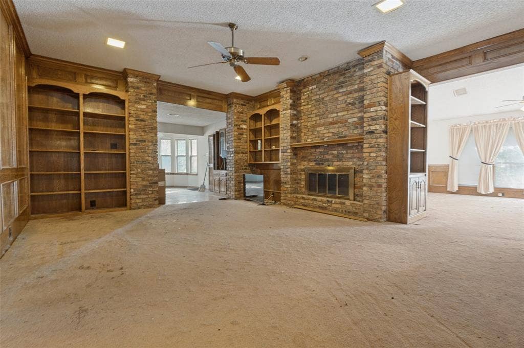 1901 Wedgewood Drive, Grand Prairie, TX 75050 Brick-clad fireplace with metal grate, built-in wooden shelving, wooden paneling, and a ceiling fan with integrated lighting