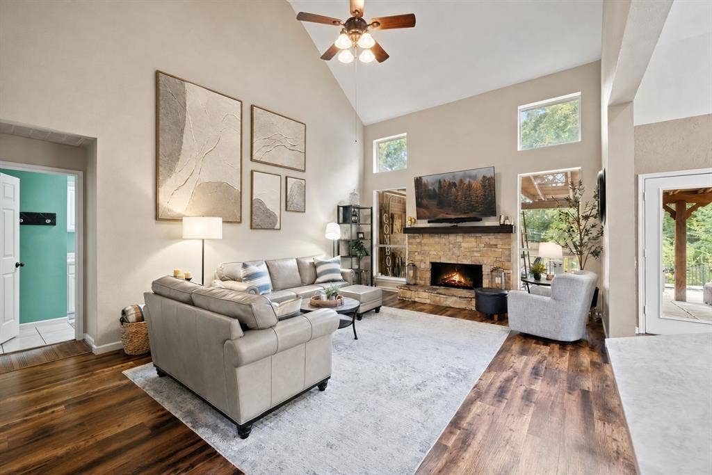 3202 Harbor Pointe Drive, Rowlett, TX 75088 Vaulted ceiling with a ceiling fan, stone-clad fireplace with a wood mantle, wood-finish flooring, and multiple high windows