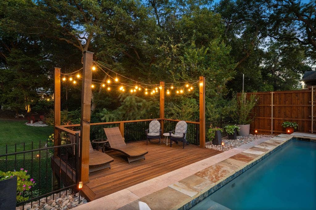 3202 Harbor Pointe Drive, Rowlett, TX 75088 Hardwood deck with string lighting, adjacent to a swimming pool with natural stone coping