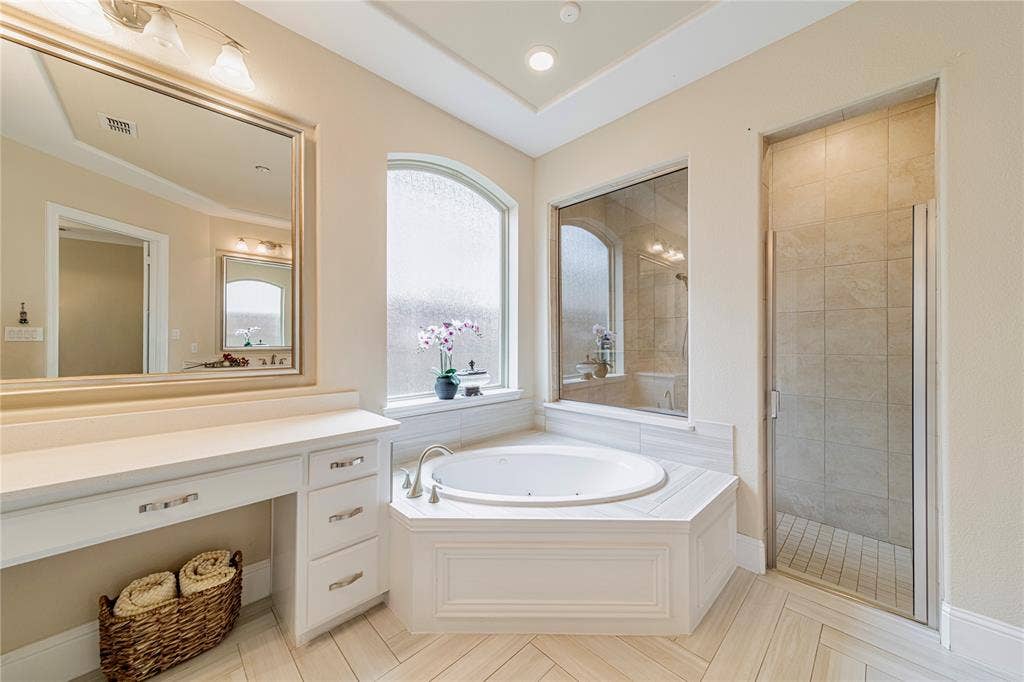 13018 Seattle Slew Street, Frisco, TX 75035 Spacious master bathroom featuring a corner jetted tub, glass-enclosed shower, a double vanity with ample counter space, and a dedicated vanity seating area and designer tile