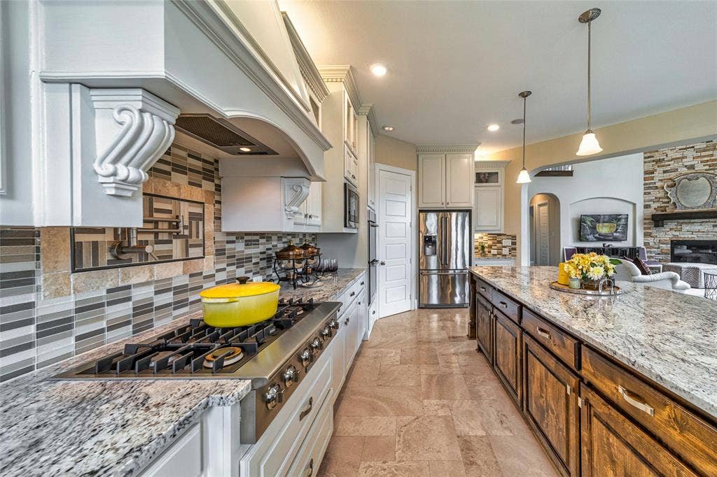 13018 Seattle Slew Street, Frisco, TX 75035 Gourmet kitchen featuring a built-in gas range, white cabinetry, a large kitchen island with wood-finish base, and stone countertops
