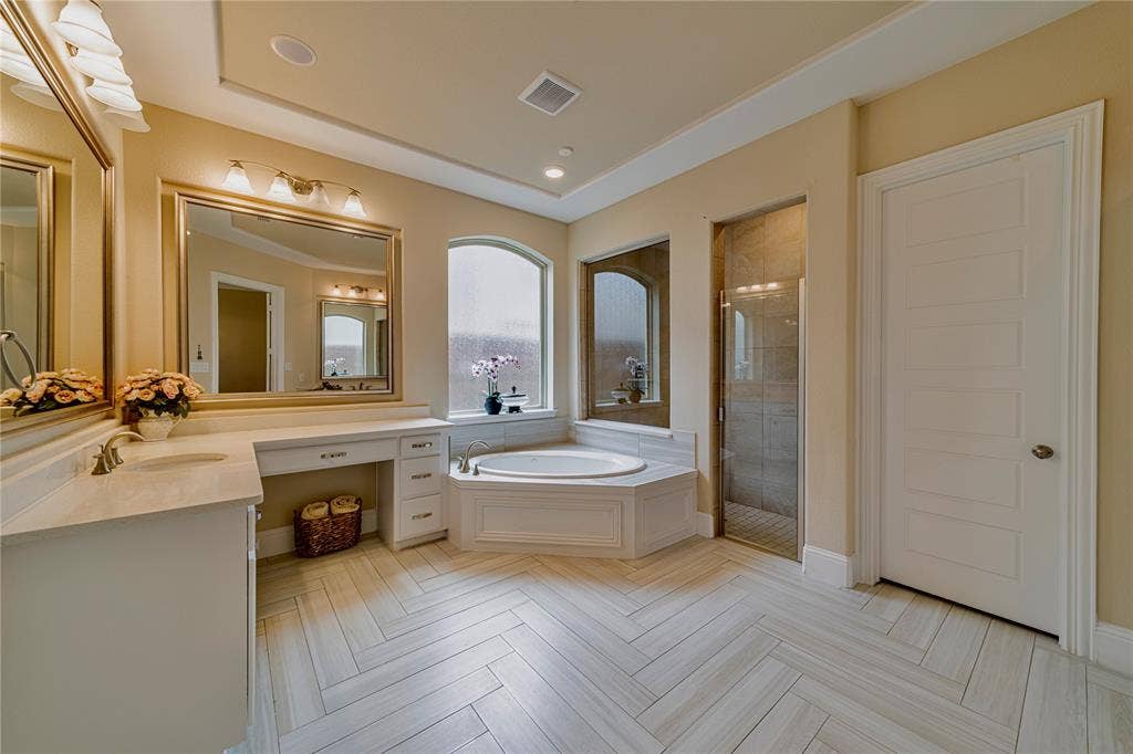 13018 Seattle Slew Street, Frisco, TX 75035 Spacious master bathroom featuring a corner jetted tub, glass-enclosed shower, a double vanity with ample counter space, and a dedicated vanity seating area and designer tile