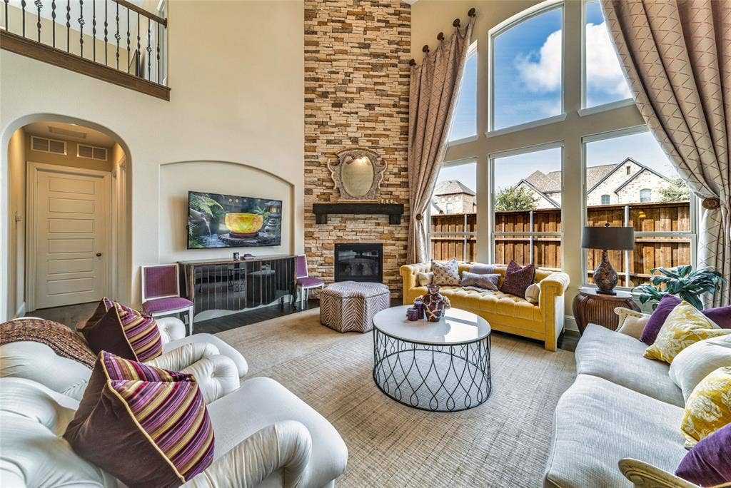 13018 Seattle Slew Street, Frisco, TX 75035 Two-story living area featuring a stacked stone fireplace, large picture windows, and a wrought iron balcony overlooking the space