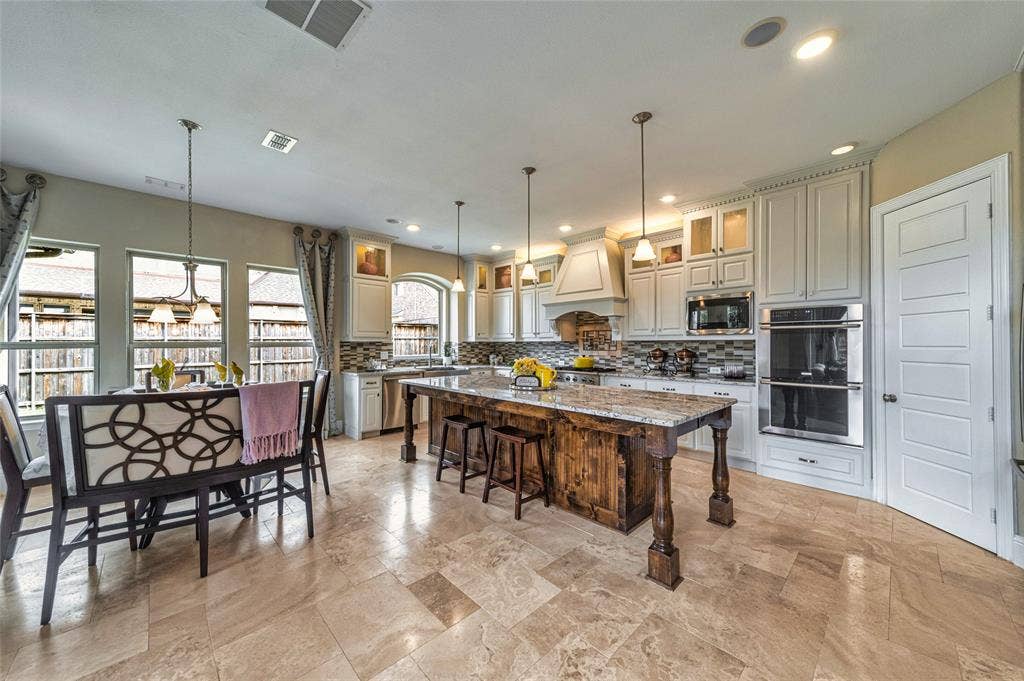 13018 Seattle Slew Street, Frisco, TX 75035 Kitchen featuring a large wood-finish island with stone countertop, white cabinetry with glass upper doors, mosaic tile backsplash, and stainless steel double ovens