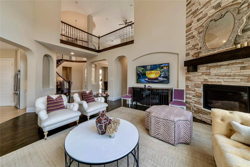 13018 Seattle Slew Street, Frisco, TX 75035 Two-story living area featuring a stone-clad fireplace, dark wood-finish flooring, and arched doorways