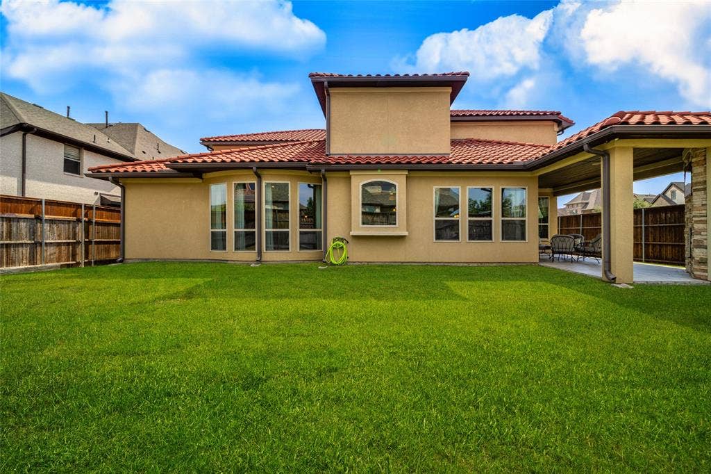13018 Seattle Slew Street, Frisco, TX 75035 Spacious grassy yard with a covered patio, stucco exterior, multiple large windows, and a terracotta tile roof