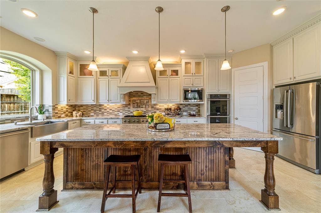 13018 Seattle Slew Street, Frisco, TX 75035 Gourmet kitchen featuring a large wood-paneled island with a granite countertop, stainless steel appliances, white customcabinetry,