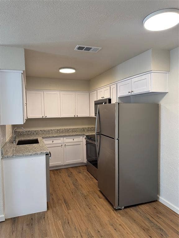 1104-1106 Mulkey Lane, Denton, TX 76209 Kitchen featuring wood-finish flooring, white cabinetry, integrated stainless steel appliances, and solid surface countertops