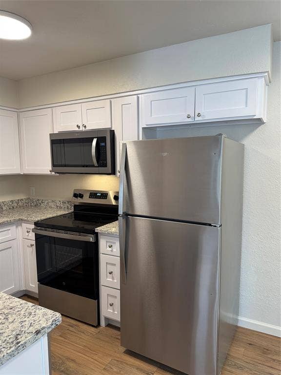 1104-1106 Mulkey Lane, Denton, TX 76209 Stainless steel appliance suite, white shaker cabinetry, speckled countertops, wood-finish flooring, and recessed lighting