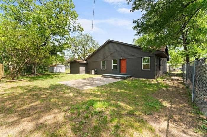 2405 Monroe Street, Commerce, TX 75428 Rear exterior with a concrete patio, dark gray siding, an orange entry door, and white window frames