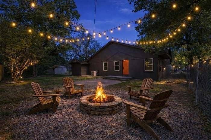 2405 Monroe Street, Commerce, TX 75428 Spacious backyard featuring a stone-clad fire pit, gravel ground cover, and a string light installation