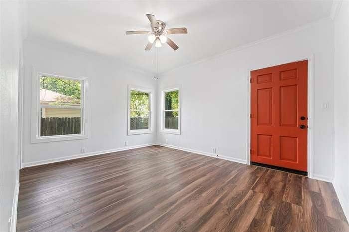 2405 Monroe Street, Commerce, TX 75428 Vibrant paneled entry door, wood-finish flooring, multiple windows, classic white trim, and a ceiling fan with integrated lighting