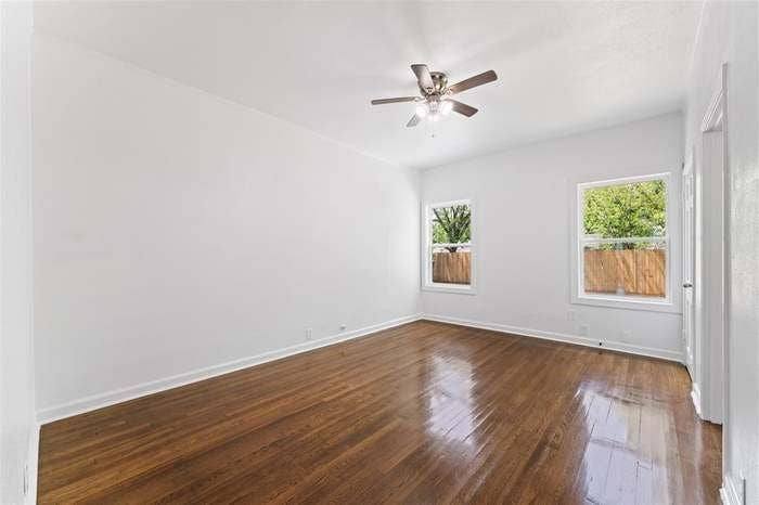 2405 Monroe Street, Commerce, TX 75428 Wood-finish flooring, two windows with white trim, a ceiling fan with integrated lighting, and a white interior door